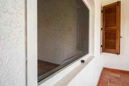 Moustiquaire en fibre de verre montée sur cadre aluminium blanc fixée sur une fenêtre méditerranéenne